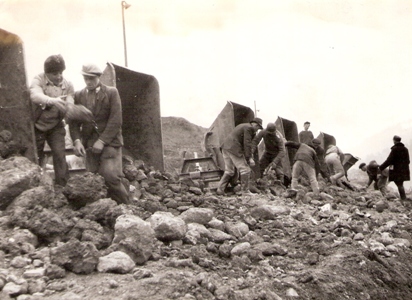  Skupina robotníkov pri vykladaní veľkých kameňov z plechových huntíkov. Text: Trať Družby. Foto: ČSD, cca 1950. 169 x 122 